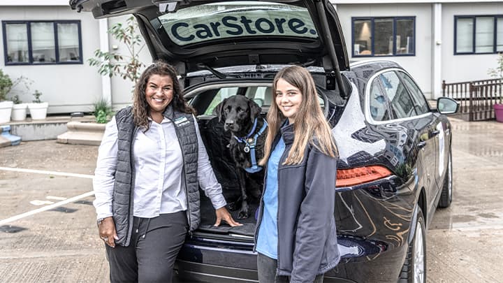 Battersea and CarStore employee standing with dog in the boot of a black car